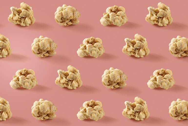 Rows of caramel popcorn clusters arranged neatly on a pink background.